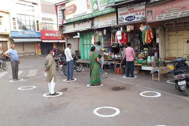 People standing in circle marked on the street with 2 meters distance between in front of grocery shop to buy necessary items